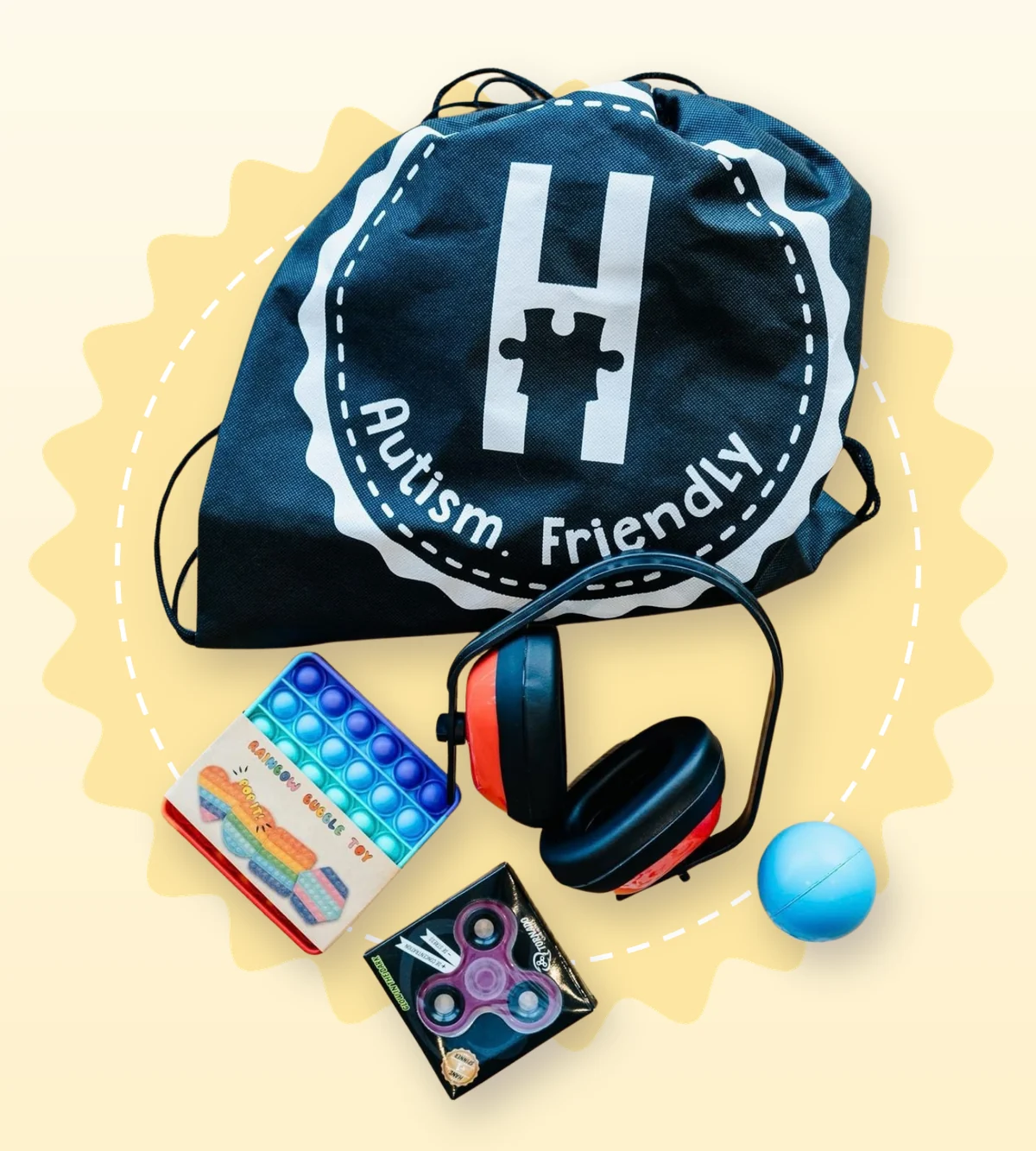 kit sensorial que consiste en una mochila negra con logo Autism Friendly, cascos reductos de ruido, un pop it, un spinner y una pelota pequeña.